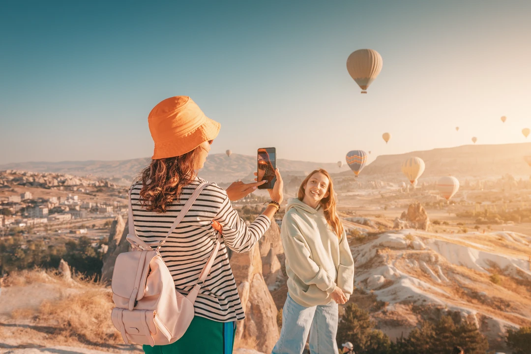2 young women in turkey at a hot air balloon festival taking photos using a smartphone